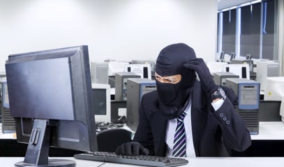 Un homme en costume avec une cagoule est assis derrière un écran d'ordinateur
