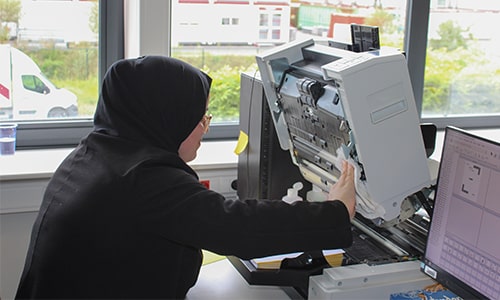 Fatima, een medewerker met hoofddoek, bedient een grote scanner in een Ze werkt nauwkeurig terwijl ze de machine controleert.