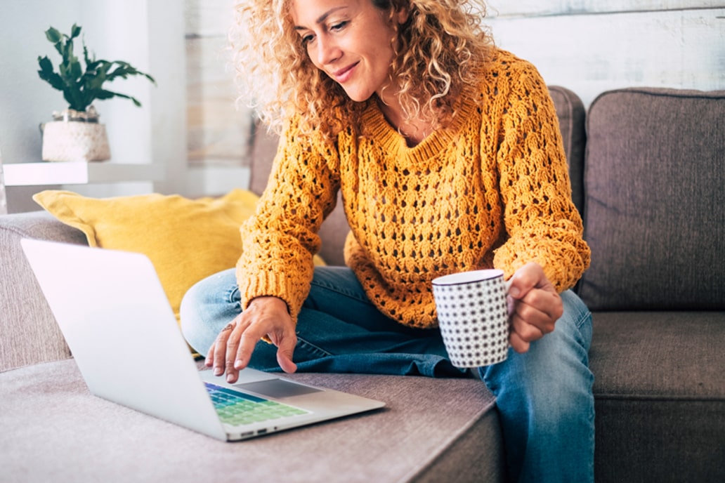 Vrouw die aan haar salontafel zit achter haar laptop, met een tas koffie